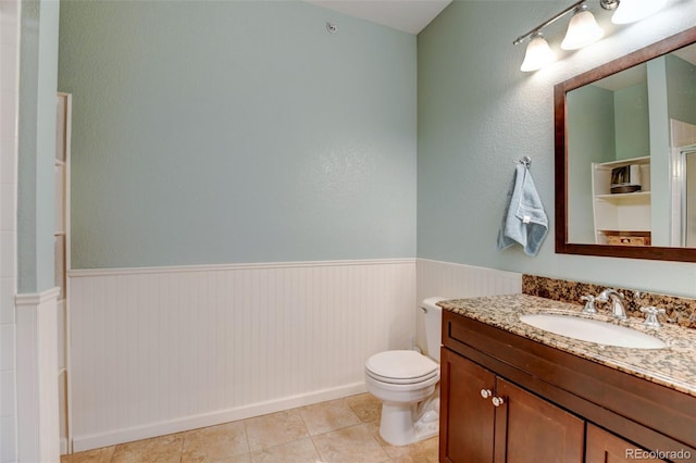 full bath featuring vanity, toilet, tile patterned flooring, and wainscoting