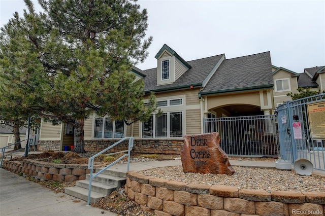 view of front of property featuring stone siding, a shingled roof, and fence