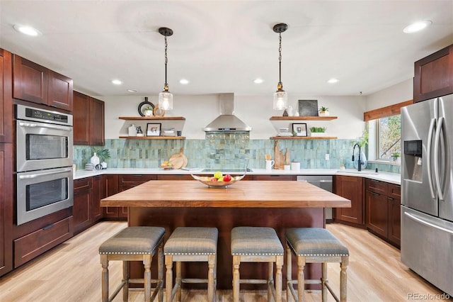 kitchen featuring open shelves, wall chimney range hood, a breakfast bar area, and stainless steel appliances