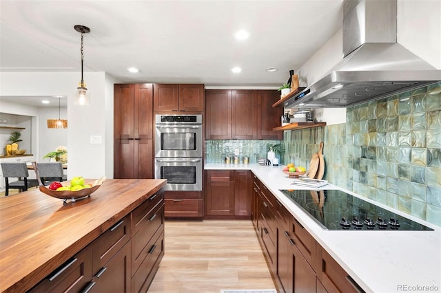 kitchen with decorative light fixtures, stainless steel double oven, wall chimney exhaust hood, butcher block counters, and black electric stovetop