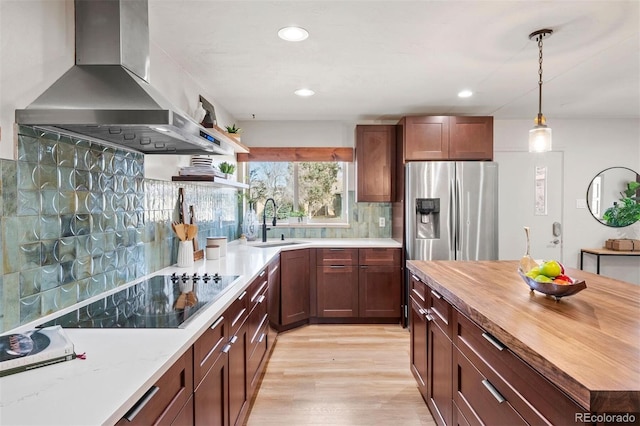 kitchen with black electric stovetop, wall chimney range hood, stainless steel fridge with ice dispenser, wood counters, and a sink