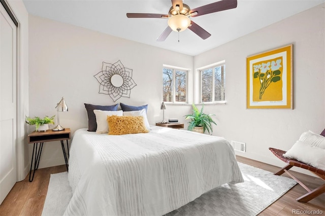 bedroom featuring visible vents, a ceiling fan, baseboards, and wood finished floors