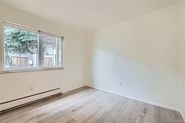 spare room featuring baseboards, light wood-type flooring, and a baseboard heating unit