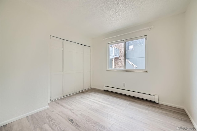 empty room featuring a baseboard radiator, baseboards, a textured ceiling, and light wood-style floors