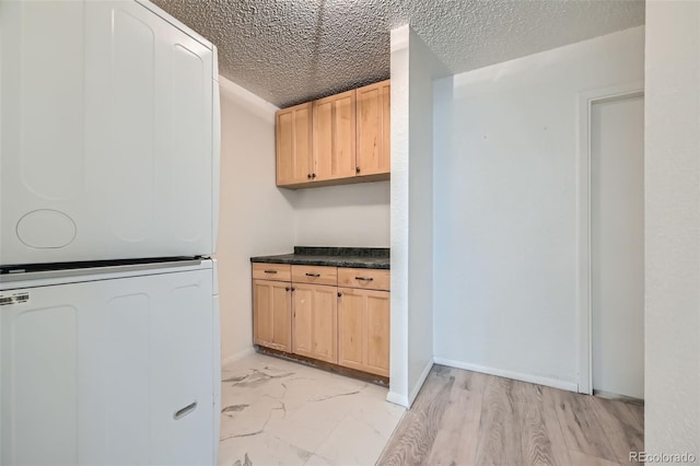 kitchen with dark countertops, stacked washer / dryer, a textured ceiling, fridge, and marble finish floor