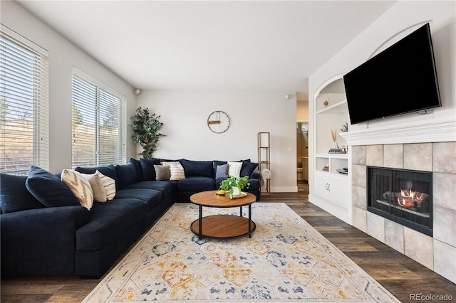 living area with baseboards, dark wood-style flooring, a tile fireplace, and built in features