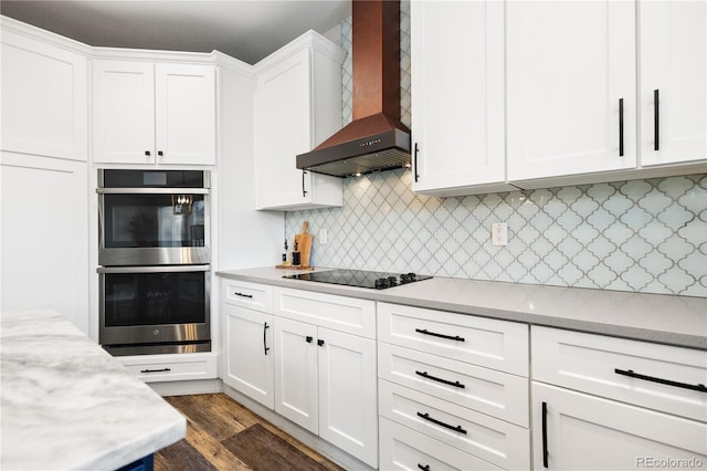 kitchen featuring double oven, black electric cooktop, premium range hood, white cabinetry, and light stone countertops