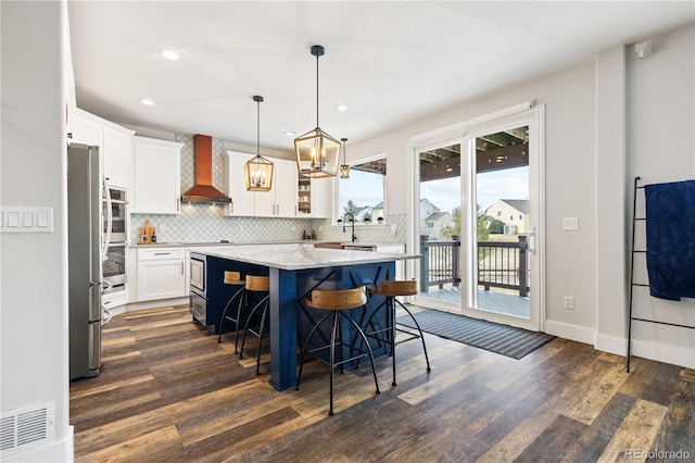 kitchen featuring wall chimney exhaust hood, decorative backsplash, a center island, and dark wood finished floors