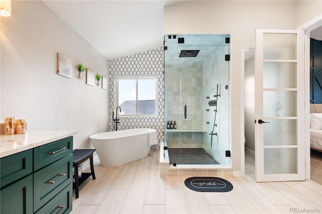 full bath featuring lofted ceiling, vanity, a freestanding bath, and a stall shower