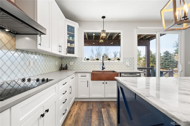 kitchen featuring dark wood-style floors, wall chimney range hood, a sink, black electric stovetop, and glass insert cabinets