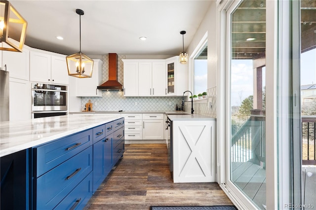 kitchen with wall chimney range hood, a sink, decorative backsplash, blue cabinetry, and white cabinetry