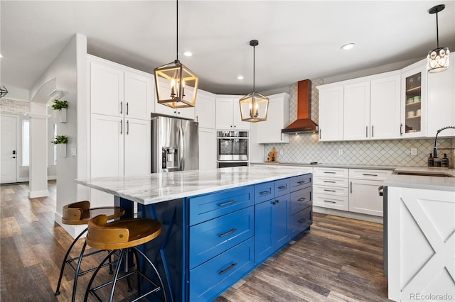 kitchen with a sink, blue cabinets, white cabinetry, wall chimney exhaust hood, and appliances with stainless steel finishes