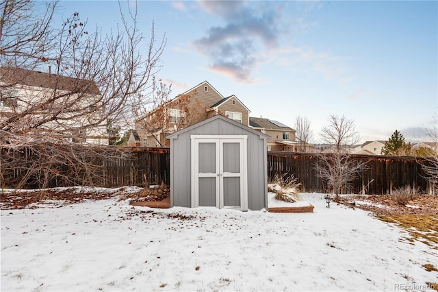 snow covered structure with a fenced backyard, an outbuilding, and a storage shed