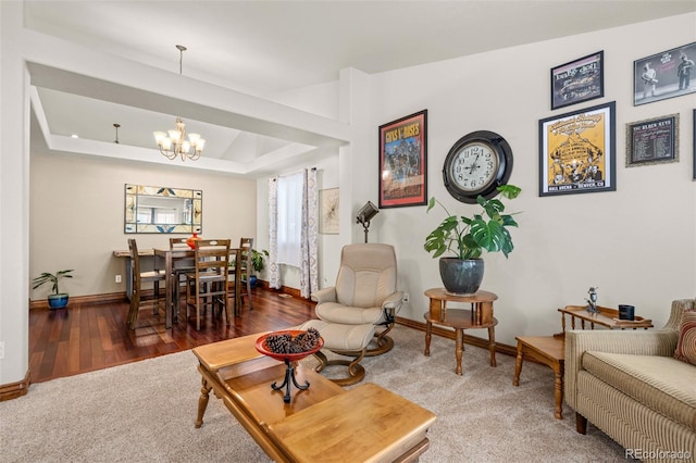 living area with an inviting chandelier, baseboards, a raised ceiling, and wood finished floors