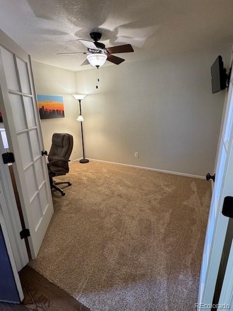 carpeted office space featuring a textured ceiling, a ceiling fan, and baseboards