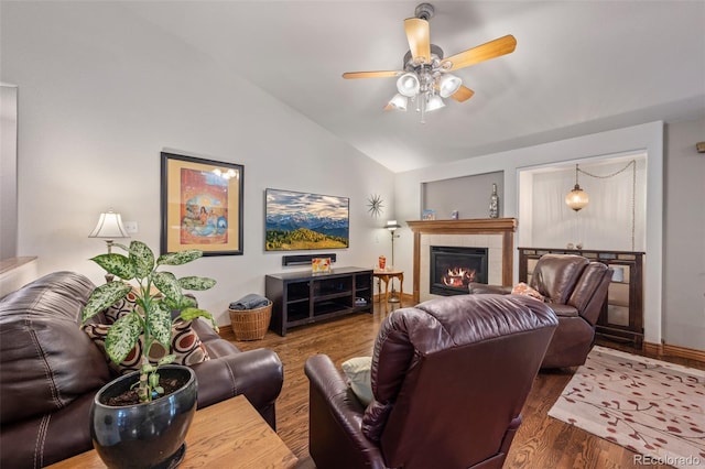 living area with baseboards, a tiled fireplace, ceiling fan, wood finished floors, and vaulted ceiling