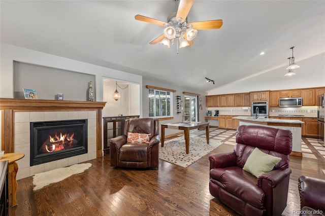 living room featuring ceiling fan, vaulted ceiling, a tile fireplace, and wood-type flooring