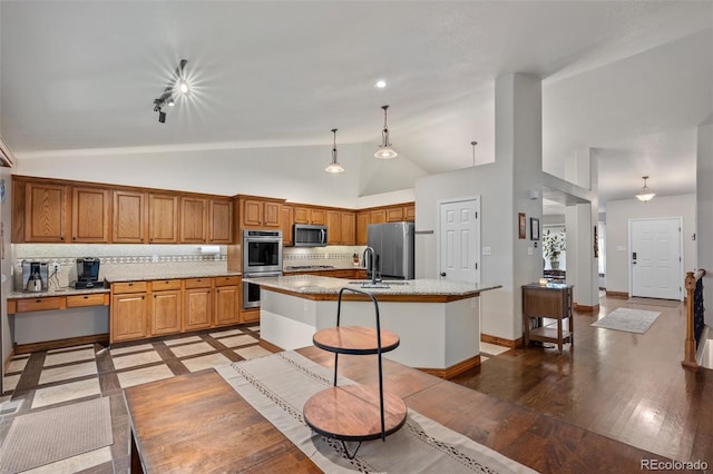 kitchen with light wood finished floors, lofted ceiling, a kitchen island with sink, stainless steel appliances, and backsplash