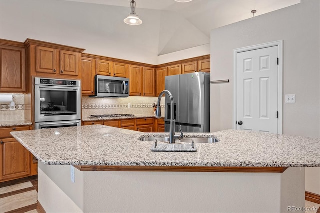 kitchen with decorative light fixtures, decorative backsplash, appliances with stainless steel finishes, and a center island with sink