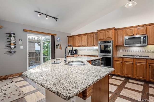 kitchen with stainless steel appliances, a sink, light stone countertops, tasteful backsplash, and brown cabinetry