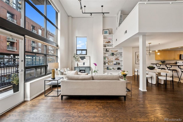 living room featuring dark wood-style floors, track lighting, a towering ceiling, and built in shelves