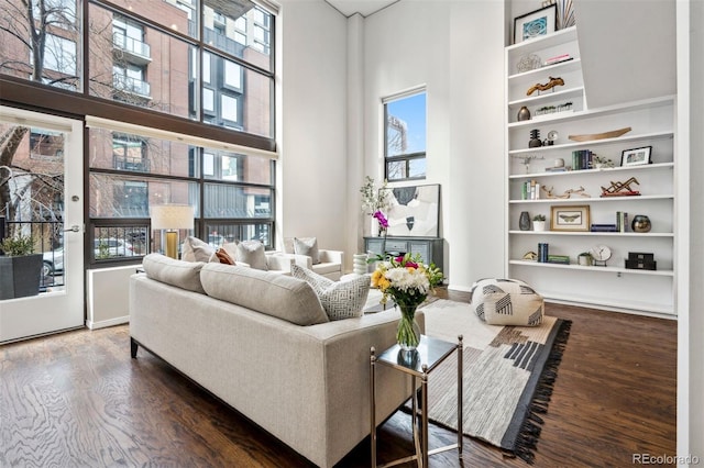 living room featuring a towering ceiling, wood finished floors, and built in shelves
