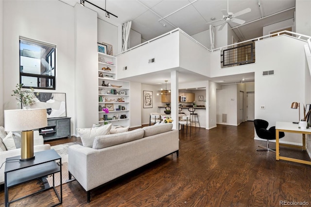 living area with a ceiling fan, a towering ceiling, wood finished floors, and built in shelves