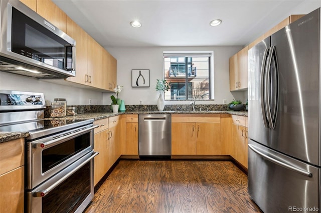 kitchen featuring appliances with stainless steel finishes, dark wood-style flooring, dark stone counters, recessed lighting, and a sink