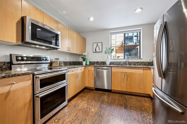 kitchen featuring appliances with stainless steel finishes, dark wood finished floors, dark stone countertops, recessed lighting, and a sink