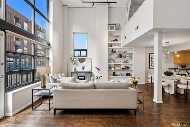 living area featuring a high ceiling, baseboards, dark wood-style flooring, built in shelves, and healthy amount of natural light