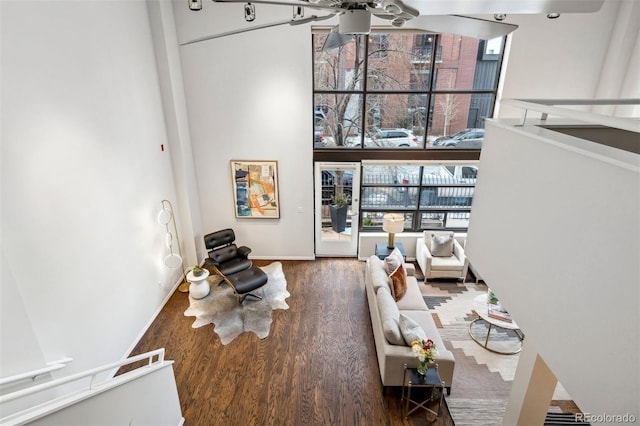 living area featuring a towering ceiling, wood finished floors, a ceiling fan, and baseboards