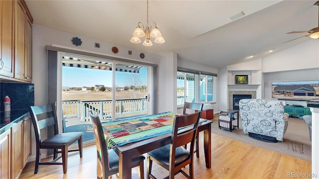 dining space with visible vents, a tiled fireplace, ceiling fan with notable chandelier, light wood finished floors, and lofted ceiling