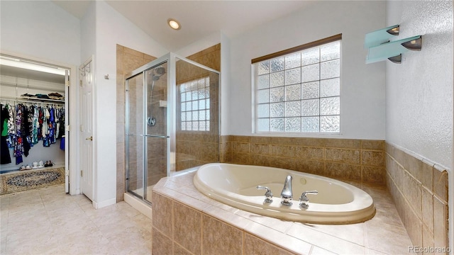 full bath featuring tile patterned flooring, a shower stall, a walk in closet, vaulted ceiling, and a bath