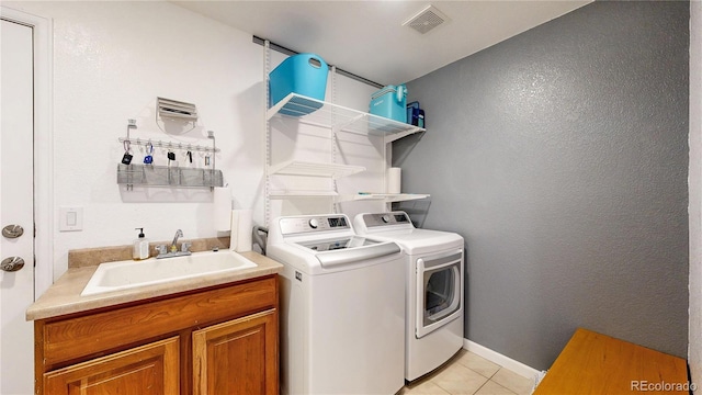 washroom featuring visible vents, a sink, washing machine and dryer, light tile patterned floors, and baseboards