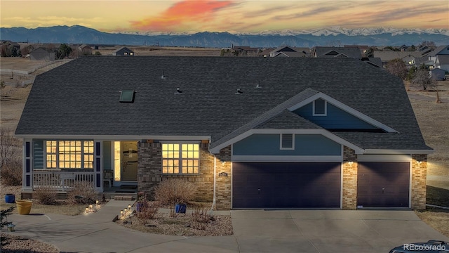 view of front of home with driveway, a mountain view, an attached garage, a shingled roof, and brick siding