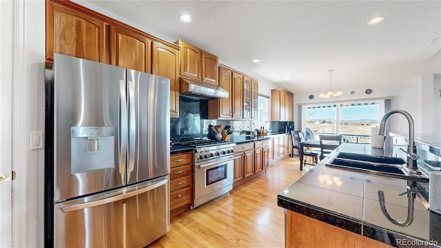 kitchen featuring an inviting chandelier, a sink, stainless steel appliances, under cabinet range hood, and brown cabinets