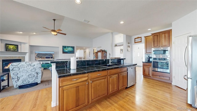 kitchen with light wood finished floors, open floor plan, appliances with stainless steel finishes, a ceiling fan, and a sink