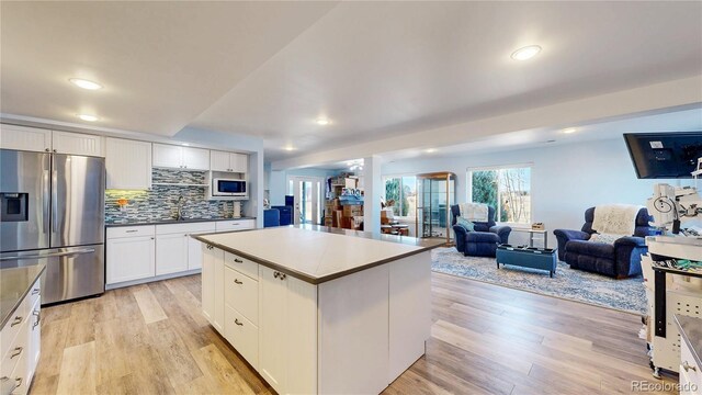 kitchen with light wood finished floors, tasteful backsplash, open floor plan, white cabinets, and stainless steel fridge