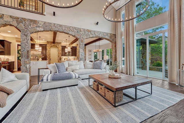 5428 Forest View Rd, Parker, CO 80134 - living area featuring arched walkways, a chandelier, a towering ceiling, wood finished floors, and decorative columns