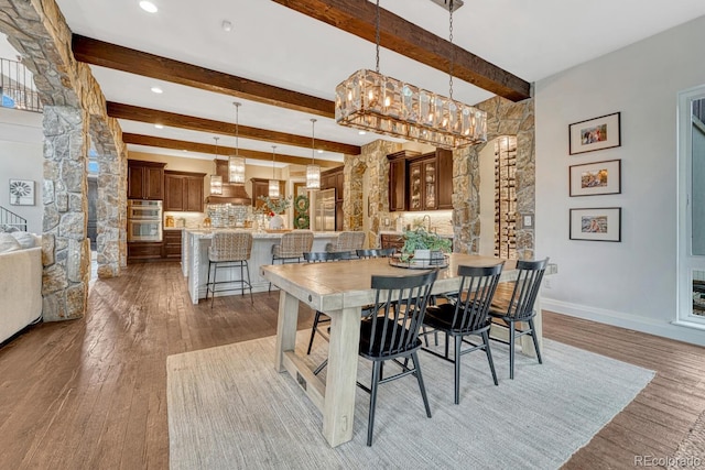 5428 Forest View Rd, Parker, CO 80134 - dining area featuring light wood finished floors, beamed ceiling, baseboards, ornate columns, and a chandelier