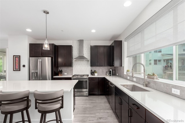 8958 Southurst St, Littleton, CO 80129 - kitchen featuring appliances with stainless steel finishes, wall chimney range hood, a sink, a kitchen breakfast bar, and light wood finished floors