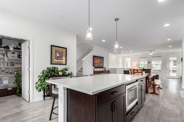 8958 Southurst St, Littleton, CO 80129 - kitchen featuring stainless steel microwave, light wood-style flooring, a center island, light countertops, and recessed lighting