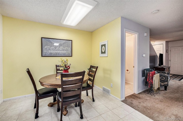 dining area with visible vents, a textured ceiling, light tile patterned floors, baseboards, and light colored carpet