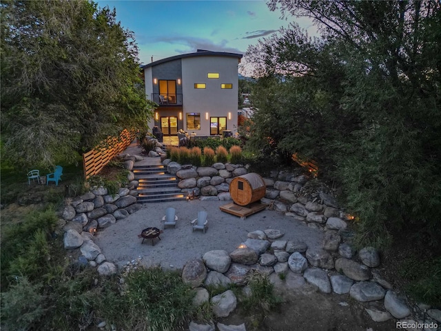 back house at dusk featuring a balcony and a fire pit