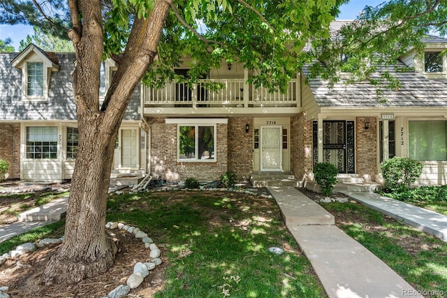 view of property featuring a front yard, brick siding, and a balcony