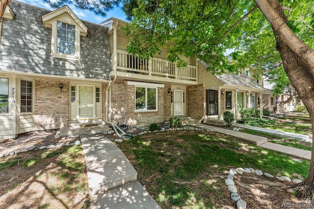 view of front of home with roof with shingles, brick siding, and a balcony