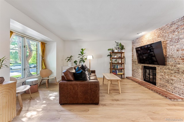 living room featuring a brick fireplace, a textured ceiling, baseboards, and wood finished floors