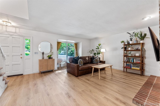 living room featuring stairs, a textured ceiling, baseboards, and light wood-style floors