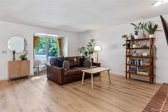 living area with light wood-type flooring, baseboards, and a textured ceiling