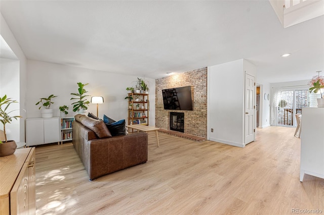 living room with light wood-style floors, a brick fireplace, and baseboards